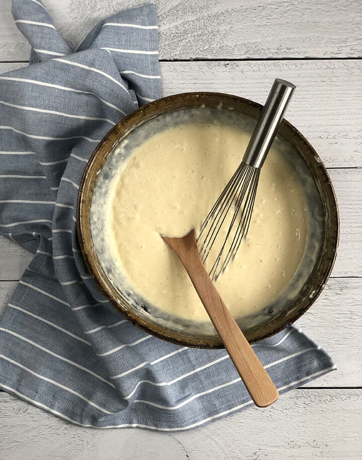 A brown bowl filled with homemade buttermilk pancake batter with a wooden spoon and a whisk resting on the bowl.