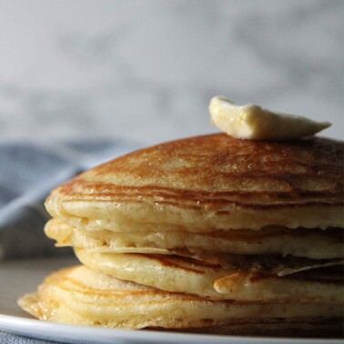 A stack of buttermilk pancakes on a plate over a blue napkin.