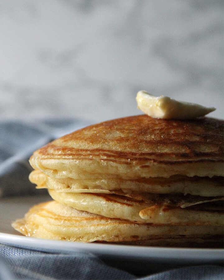 A stack of buttermilk pancakes on a plate over a blue napkin.