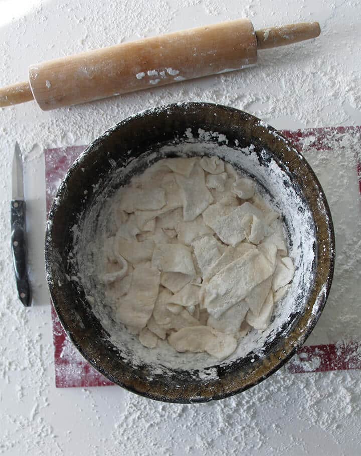 Sliced dumplings in a brown bowl with a rolling pin on the counter.