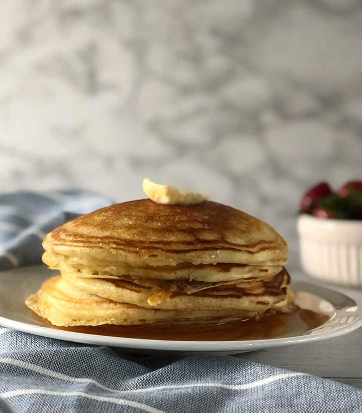 A stack of homemade buttermilk pancakes on a white plate with a blue towel on the side.