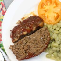 Southern meatloaf on a plate with butter beans and tomatoes.