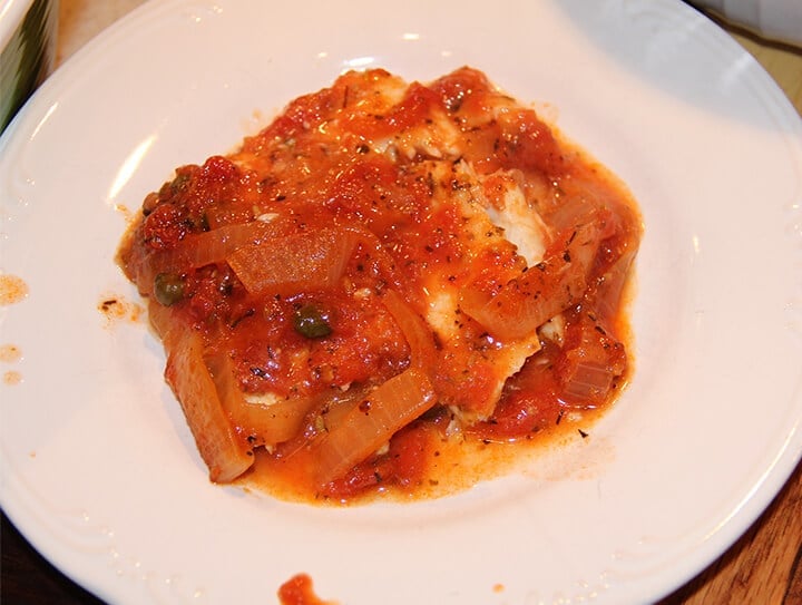 A white plate with Mediterranean fish with tomatoes and onions.