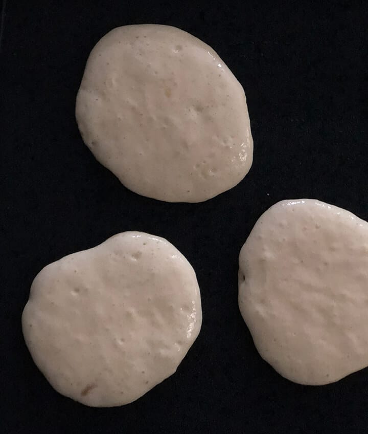 Three buttermilk pancakes cooking on a griddle.