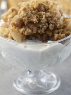 A glass dish of easy apple crisp without oats on top of vanilla ice cream.