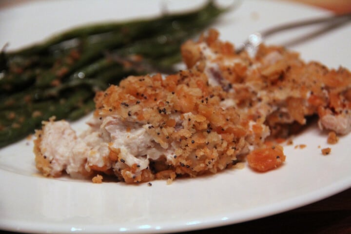 A serving of poppy seed chicken casserole on a white plate with green beans.