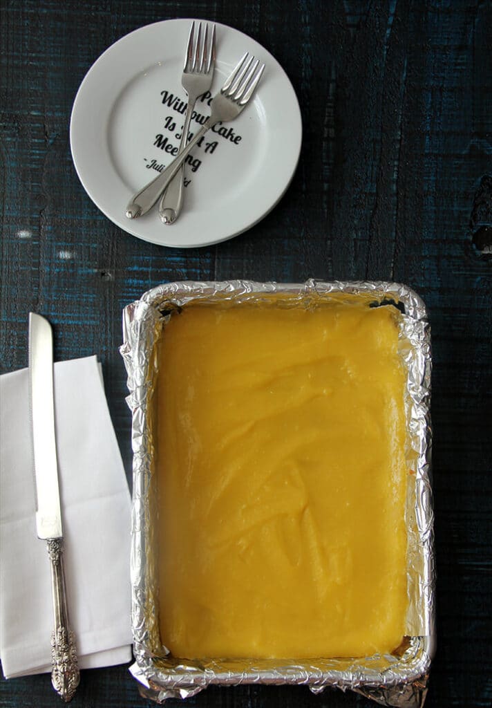 Baked lemon bars in a foil lined pan next to a white towel.