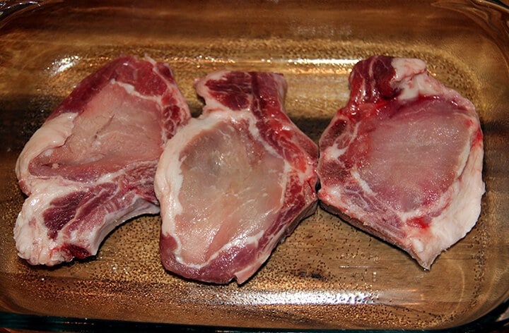 Three raw pork chops in a glass baking dish.