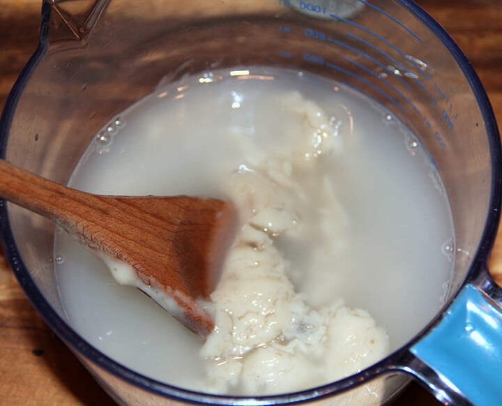 A glass mixing bowl with cream of mushroom soup and water stirred with a wooden spoon.