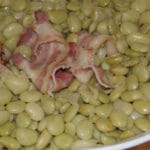 A white bowl filled with cooked butter beans and bacon.