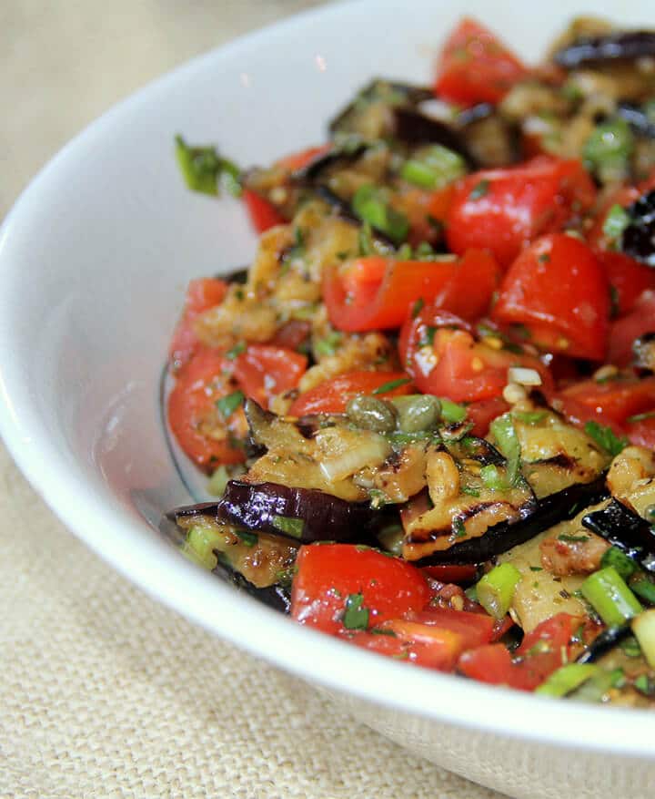 Side view closeup of grilled eggplant salad in a white bowl on burlap.