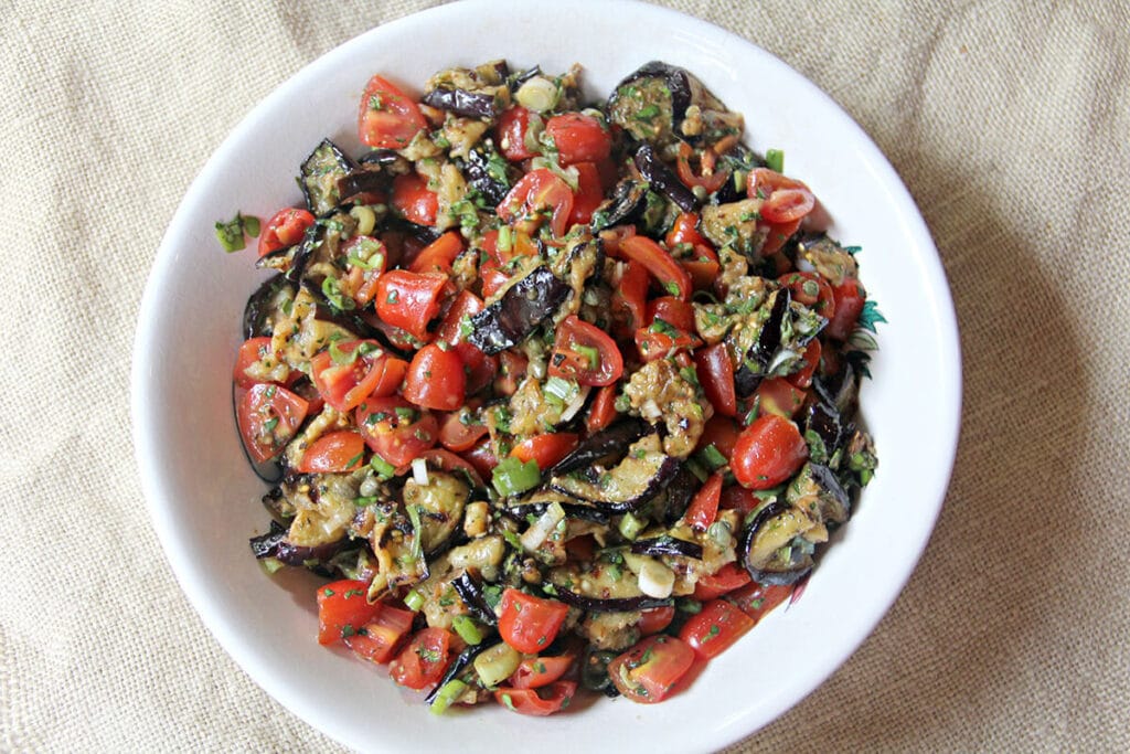 A white bowl filled with grilled eggplant salad on a burlap background.