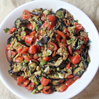 A white bowl filled with grilled eggplant salad on a burlap background.