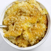A white dish filled with squash casserole with crumbled Ritz crackers.