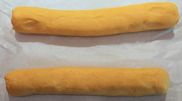 Rolls of cheese straw dough to be sliced on parchment paper.