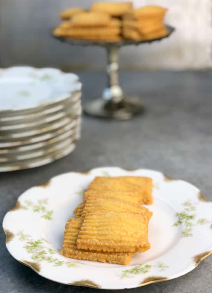 Cheese straws on a plate with a platter of more in the background.