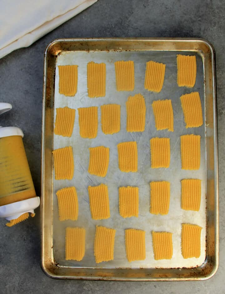 Cheese straws pressed on a baking sheet next to the cookie press.