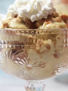 A clear glass bowl of banana pudding topped with whipped cream.