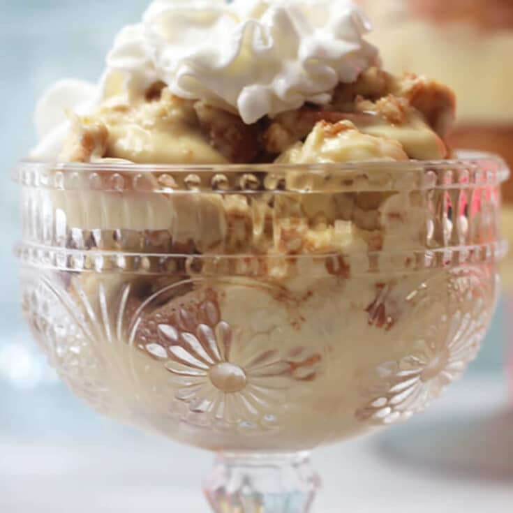 A clear glass bowl of banana pudding topped with whipped cream.