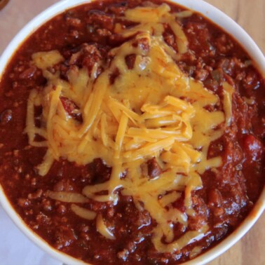 A white bowl of classic beef chili topped with grated cheese.