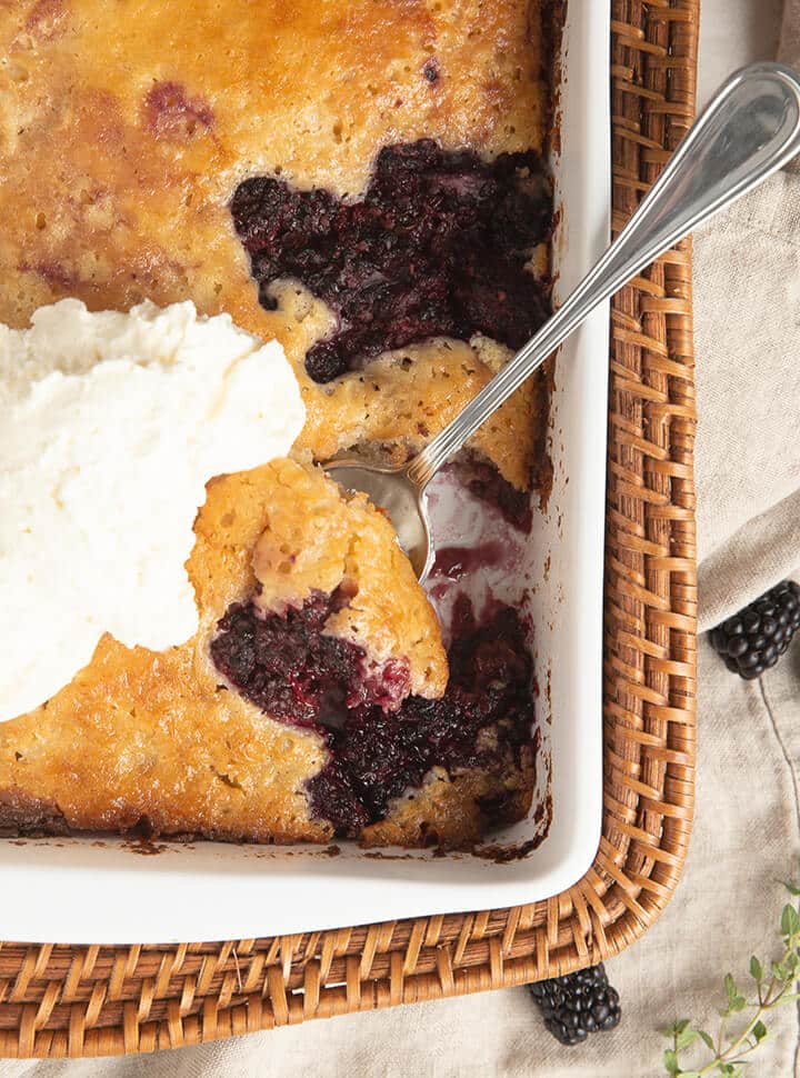 Baked blackberry cobbler in a white dish with a spoon.