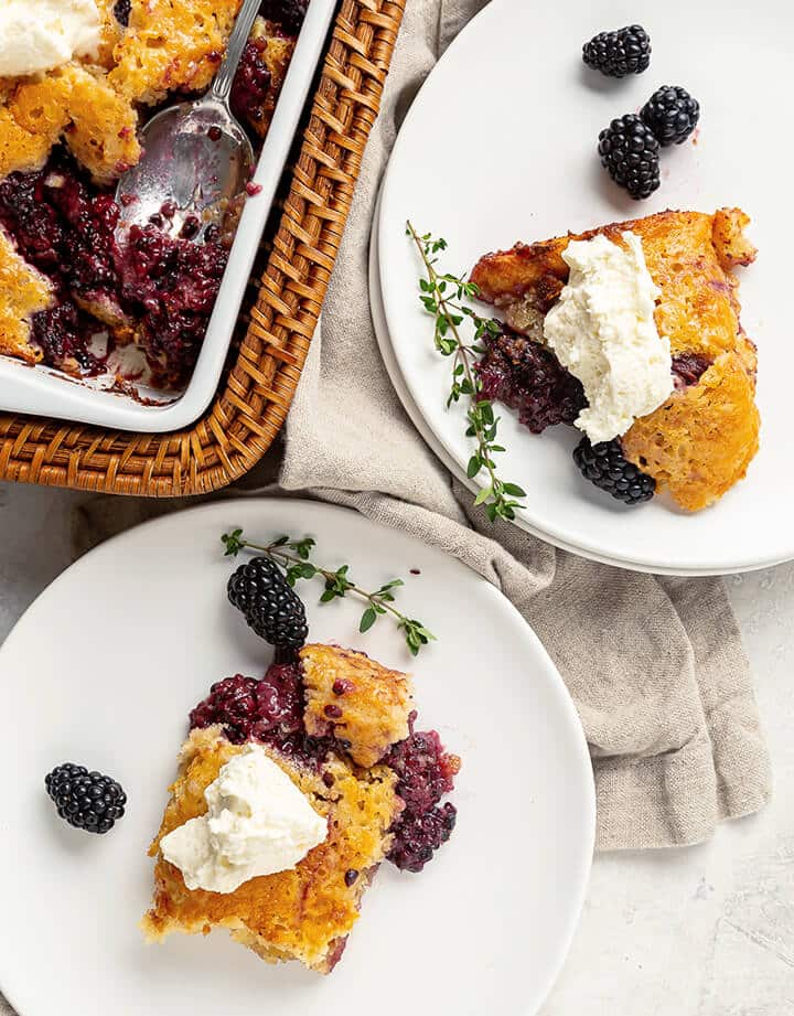 Two white plates with servings of blackberry cobbler with whipped cream.