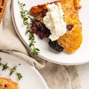 A serving of blackberry cobbler with whipped cream on a white plate.