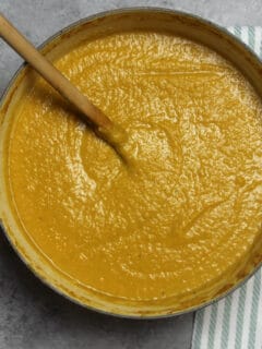 Butternut Squash Soup in a large pot on a grey board with a striped towel.