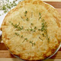 Double crust chicken pot pie on a cutting board with fresh thyme.