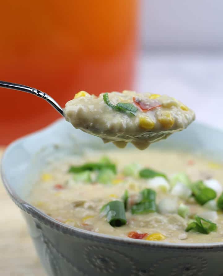 A spoonful of chicken corn chowder over a blue bowl.