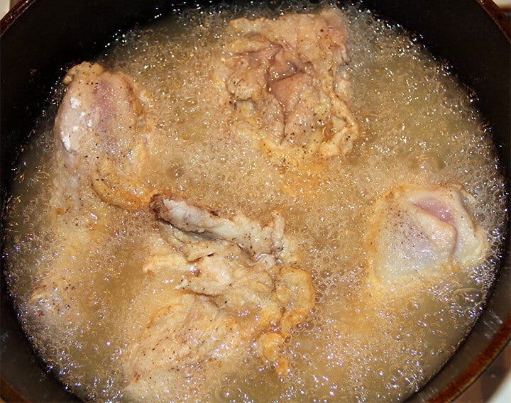 Chicken pieces frying in oil in a skillet.