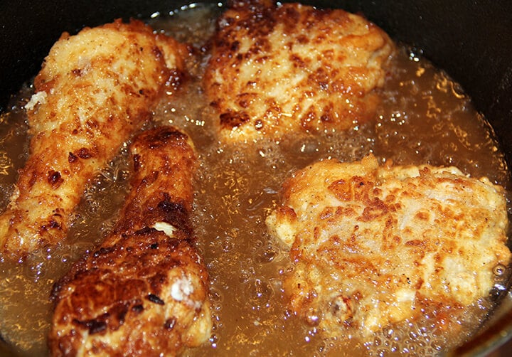 Lightly browned chicken frying in a cast iron skillet.