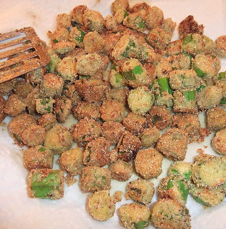 Fried okra on paper towels on a plate with a spatula on it.