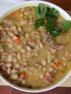 A white bowl filled with navy bean and ham soup with a sprig of parsley.