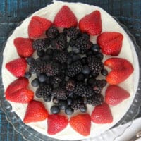 Red white and blue cake with strawberries and blueberries on a blue background.
