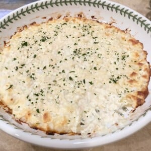 A large white bowl with green border filled with vidalia onion dip sprinkled with parsley.