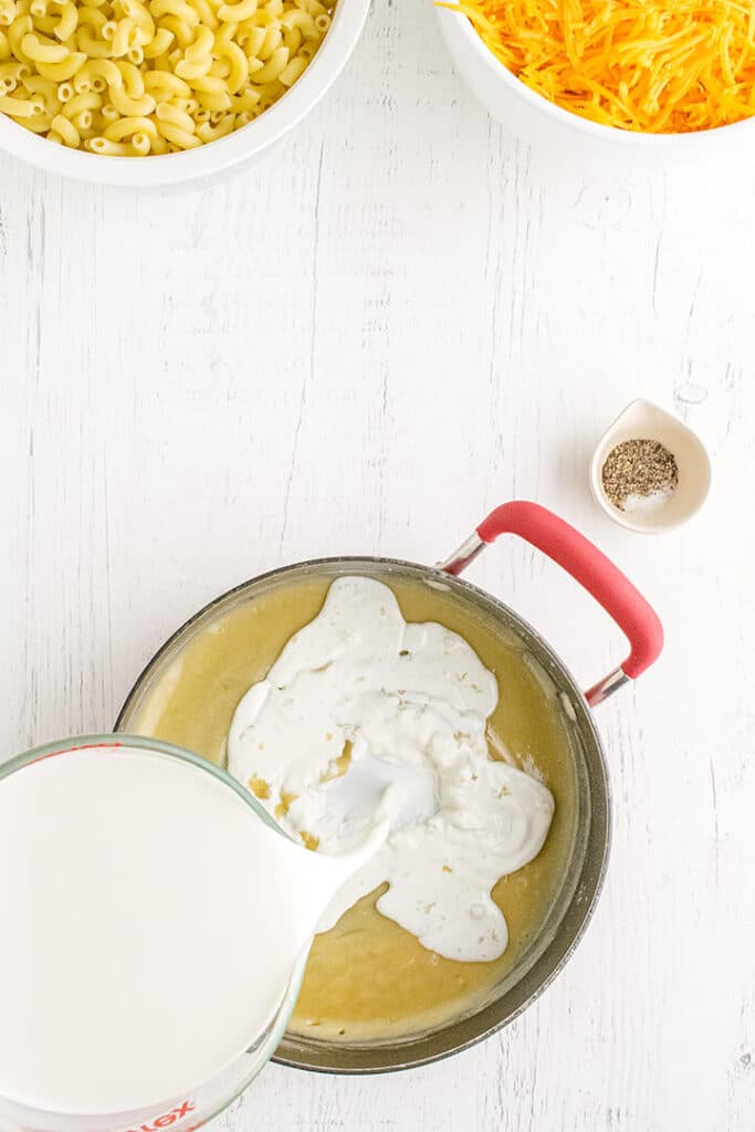 A pot of roux with half and half pouring in on a white background.