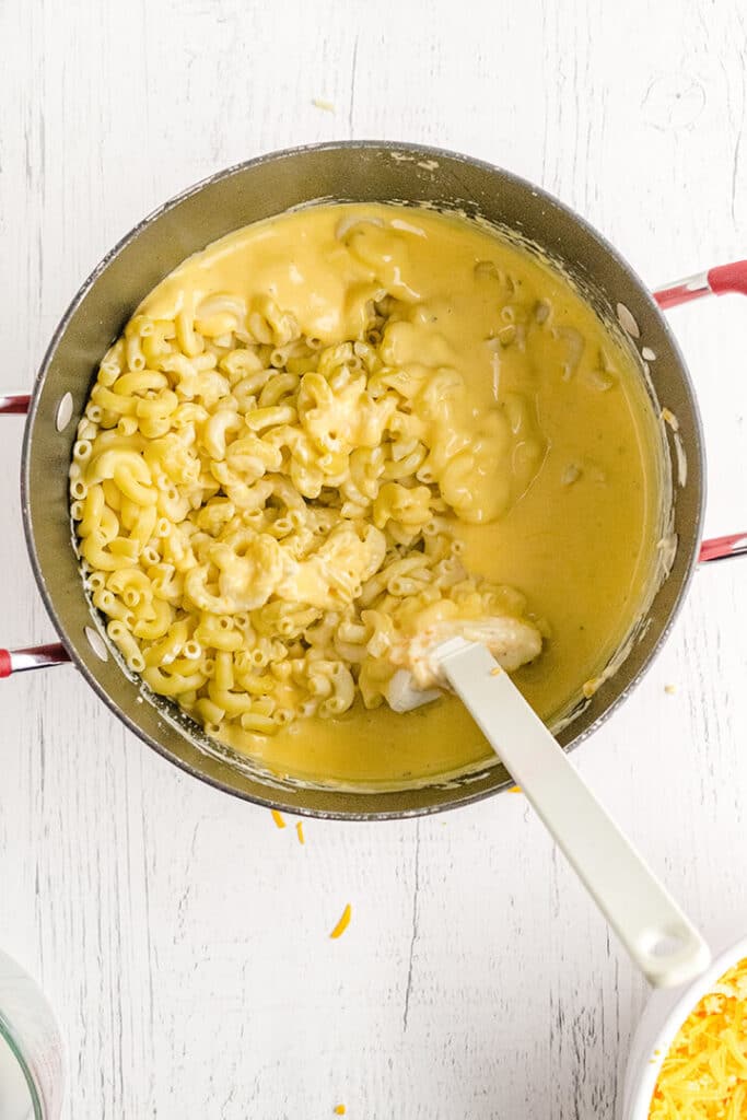 Adding noodles to cheese sauce in a pot with a white spoon.