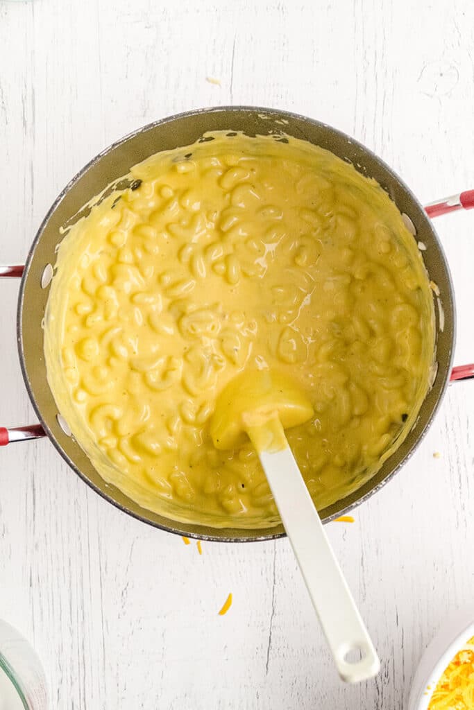 Creamy mac and cheese in a stainless pot with a white spoon.