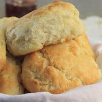 Closeup of buttermilk biscuits in a basket with a white towel.