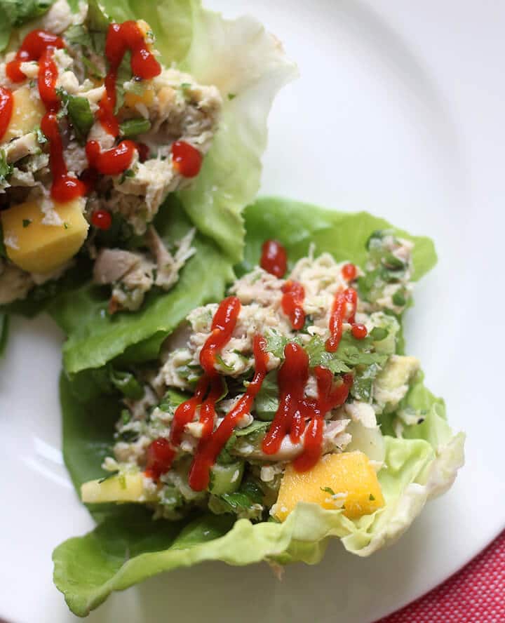 Closeup of chicken lettuce wraps on a white plate with a drizzle of Sriracha sauce.