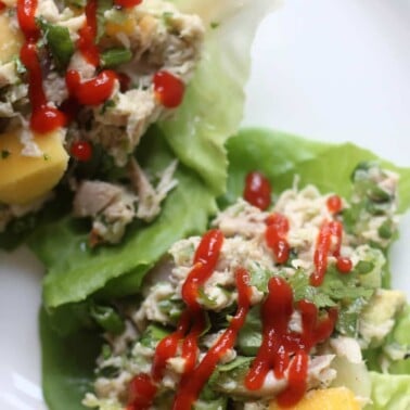 Closeup of chicken lettuce wraps on a white plate with a drizzle of Sriracha sauce.