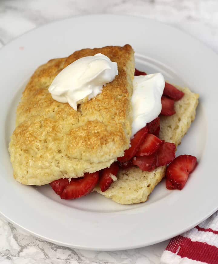 Closeup of strawberry shortcake with strawberries and whipped cream on a white plate.