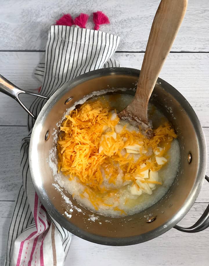 A pot of grits with grated cheese and butter and a wooden spoon.
