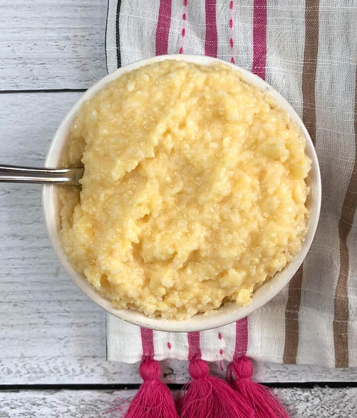 Cheese grits in a white bowl on a striped towel.