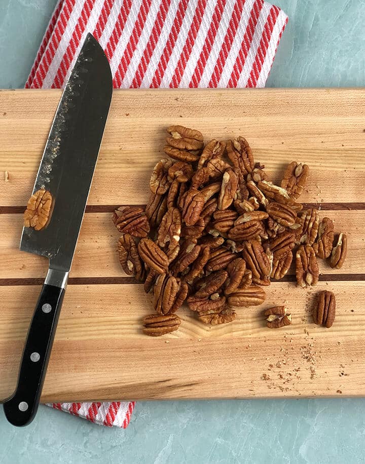 Pecans on a cutting board next to a knife.