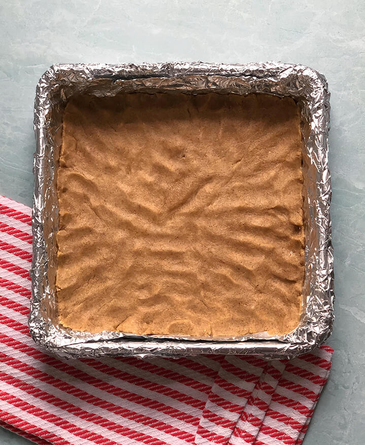 Crust for pecan pie bars in prepared pan on foil to bake.