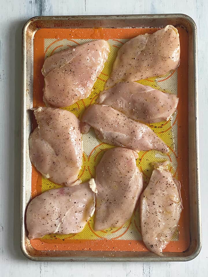 Chicken breasts drizzled with olive oil and salt and pepper on a baking sheet.