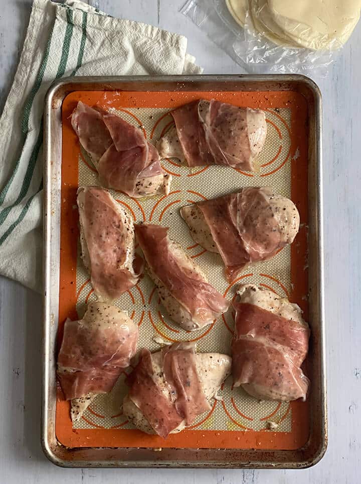 Prosciutto slices on chicken breasts on a baking sheet.