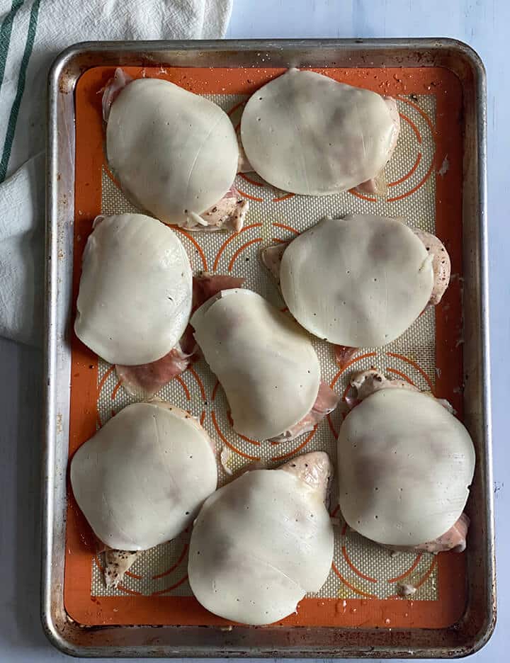 Provolone cheese on top of chicken breasts on a baking sheet.